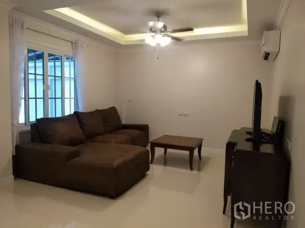 联排别墅 出租在Mueang Samut Prakan, Samut Prakan - 舒适客厅，L形沙发、吊扇与嵌灯，配电视柜。