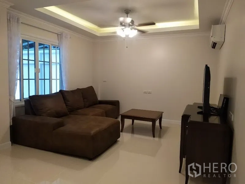 联排别墅 出租在Mueang Samut Prakan, Samut Prakan - 舒适客厅，L形沙发、吊扇与嵌灯，配电视柜。