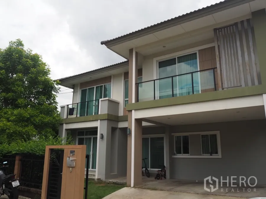 Detached House for rent in Pathum Thani - Two-storey detached house with balcony, covered carport, gated entry and mature trees.