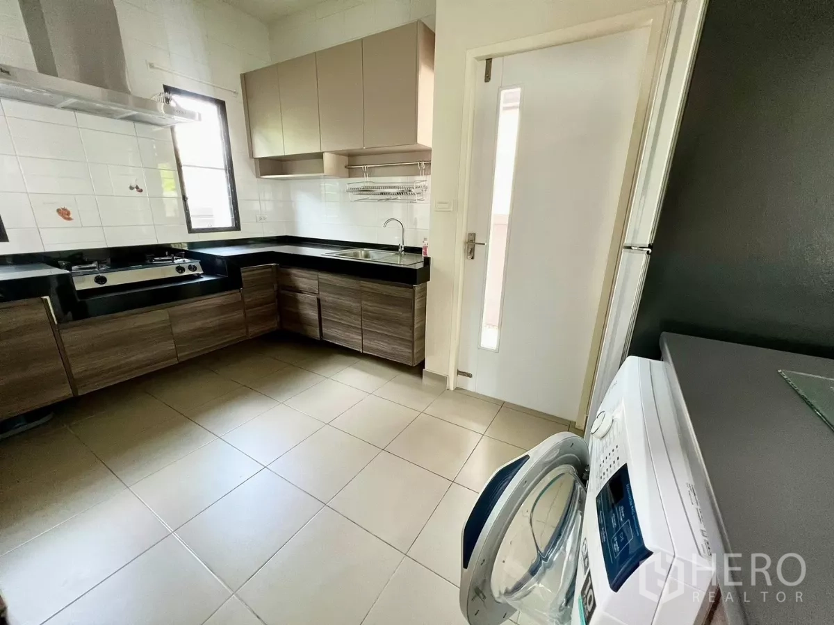 Detached House for rent or sale in Bang Phli, Samut Prakan - Separate kitchen with L-shaped counters, gas hob, range hood, sink and laundry area.