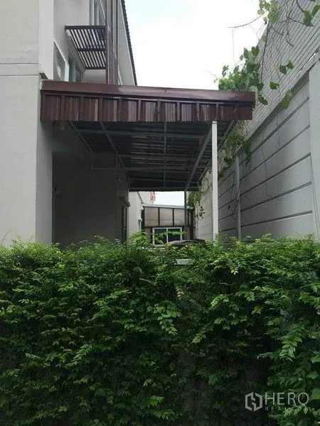 ทาวน์เฮาส์ ขายในSuan Luang, Bangkok - พื้นที่ข้างบ้านมีกันสาดโลหะและกำแพงกันชนปกคลุมเถาวัลย์สีเขียว