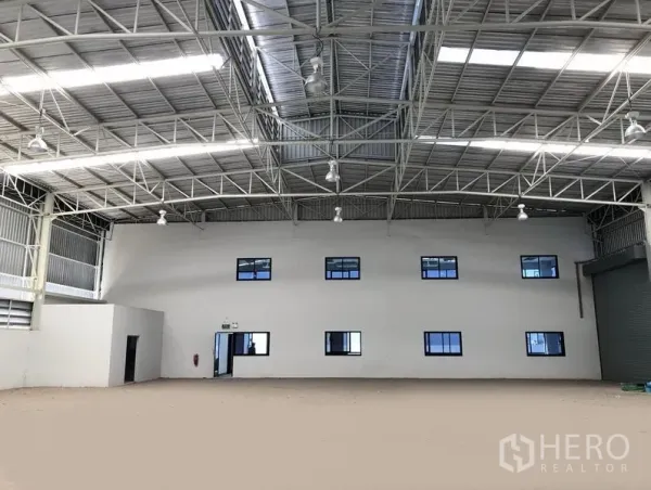 工厂 出租或出售在Bang Sao Thong, Samut Prakan - 仓库内朝向两层办公楼立面，高钢梁屋顶，右侧设卷帘门。