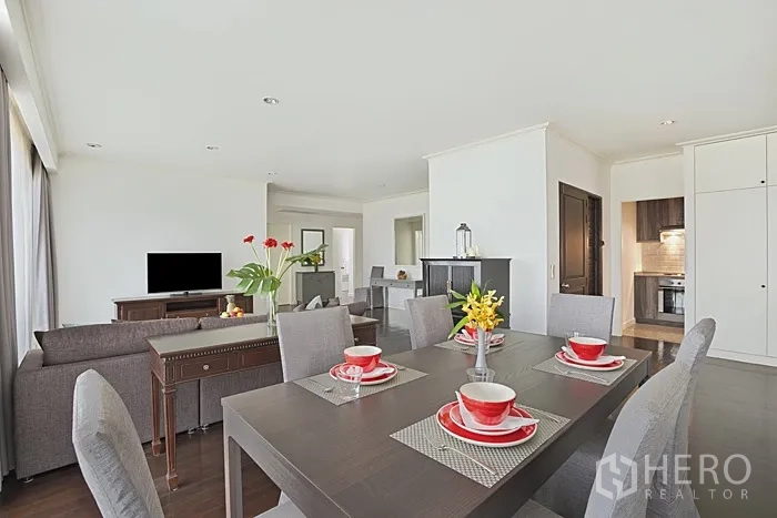 Condominium for rent in Khlong San, Bangkok - Open-plan dining and living area with gray chairs, TV and abundant natural light, connected to the kitchen.