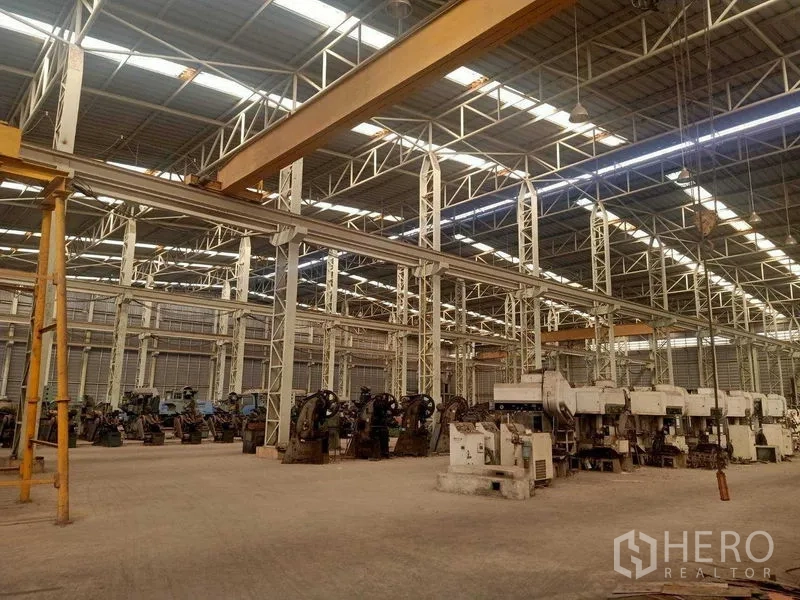 Warehouse for rent in Mueang Samut Sakhon, Samut Sakhon - Industrial hall with multiple yellow overhead cranes and rows of large machines.