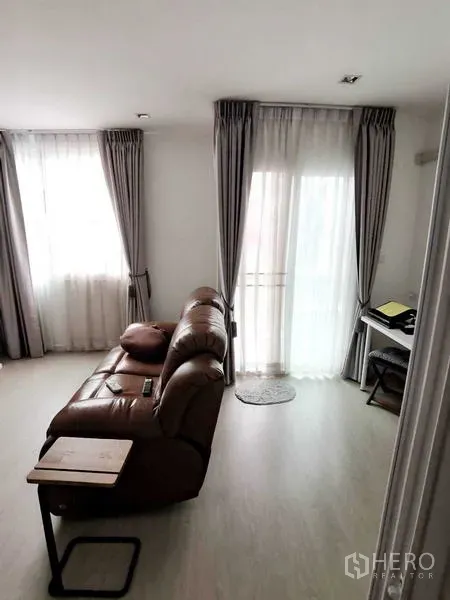 Home Office for rent or sale - Cozy lounge with a leather sofa, full-height curtains and a door to the balcony.