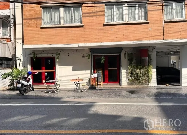 零售空间 出租在Watthana, Bangkok - 临街店面外观，红色门面与户外桌椅，带遮棚车位，位于Watthana