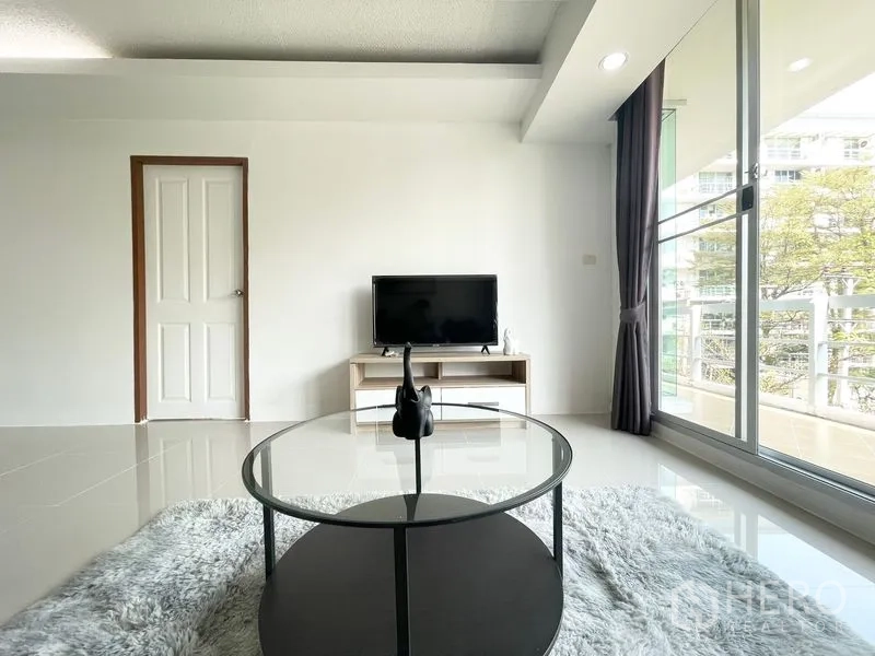 คอนโด for rent in Khlong Toei, Bangkok - ห้องนั่งเล่นมีชั้นวางทีวีและโต๊ะกลางกลมติดประตูกระจกบานเลื่อน