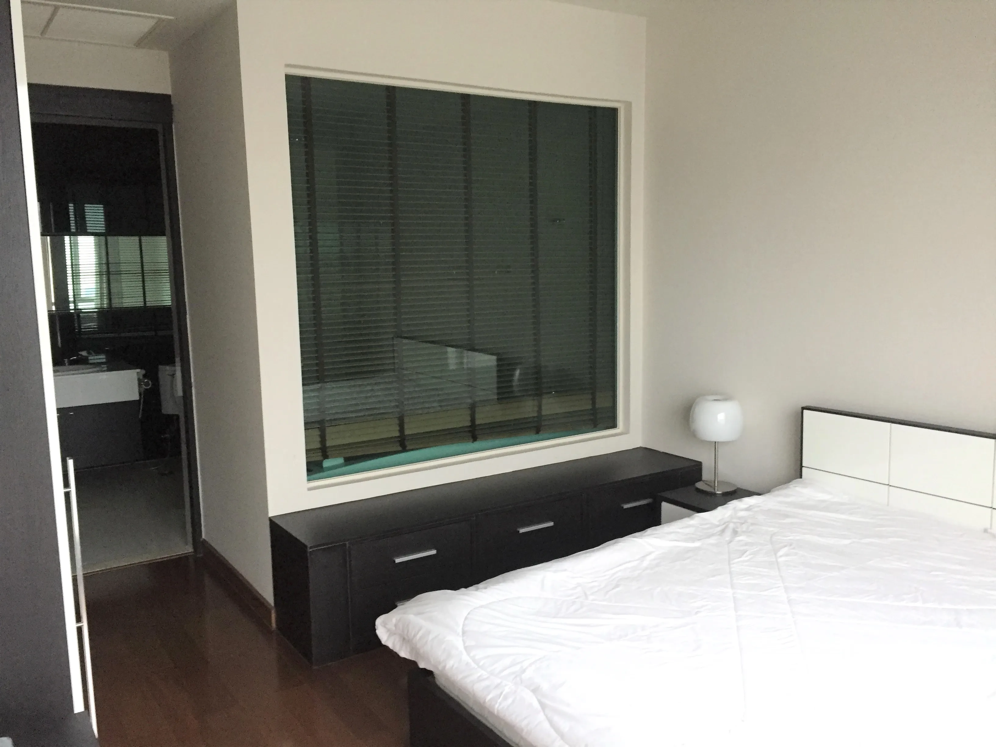 คอนโด ให้เช่าหรือขายในPathum Wan, Bangkok - ห้องนอนอบอุ่น มีหน้าต่างกระจกบานใหญ่ ตู้ลิ้นชักบิลท์อิน และโคมไฟ ข้างๆ เป็นห้องน้ำสมัยใหม่