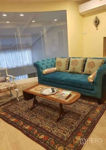 Townhouse for sale in Yan Nawa, Bangkok - Cozy sitting area with teal tufted sofa, ornate rug, coffee table and glass partition.