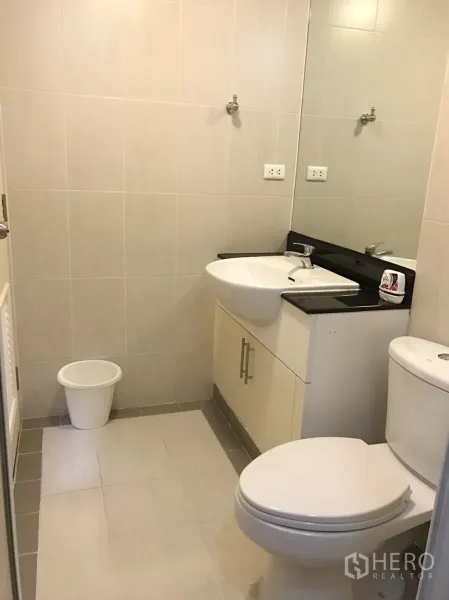 Condominium for rent in Watthana, Bangkok - Tiled bathroom with vanity, wide mirror, sink and toilet.