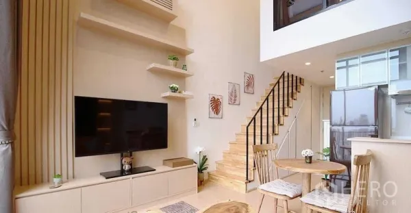 Condominium for rent in Watthana, Bangkok - Double-height living room with TV wall, open staircase and compact dining nook.