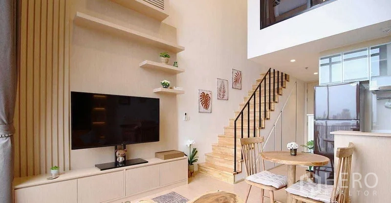 Condominium for rent in Watthana, Bangkok - Double-height living room with TV wall, open staircase and compact dining nook.