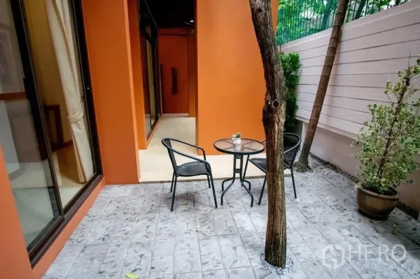 Townhouse for rent in Watthana, Bangkok - Private patio with bistro table, tree, and orange exterior walls.