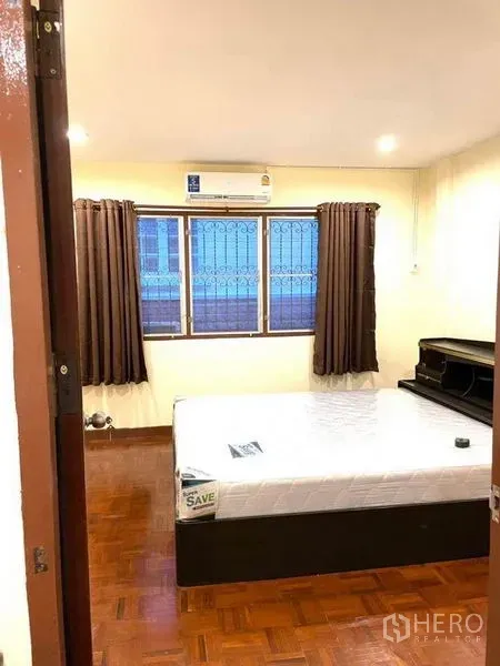 联排别墅 出租在Bang Na, Bangkok - 卧室明亮，拼花木地板，双人床，空调与带护栏的窗户。