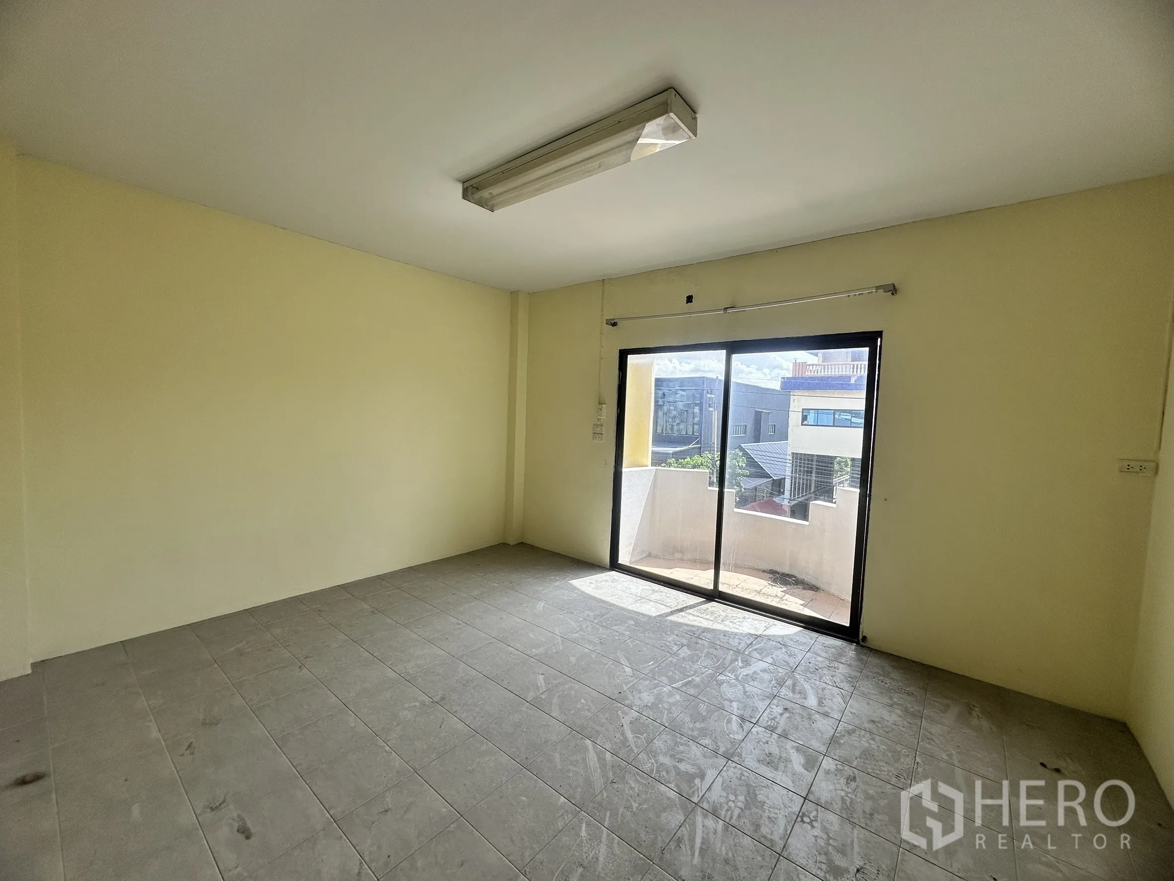 Factory for sale in Bang Bua Thong, Nonthaburi - Empty tiled office room with sliding glass doors opening to a small balcony.