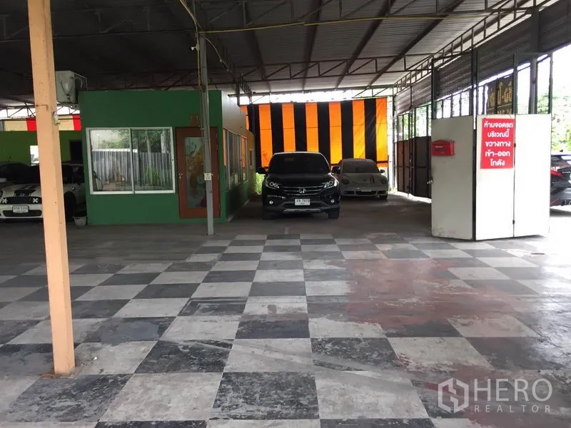 Warehouse for rent in Pathum Thani - Central aisle with checkered tiles, partition walls and an orange‑black curtain.