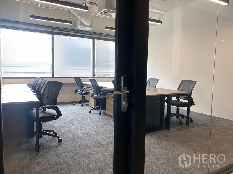 สำนักงาน ให้เช่าในUthai, Phra Nakhon Si Ayutthaya - มุมมองผ่านประตูกระจกสู่ออฟฟิศสว่าง พื้นพรม โต๊ะทำงานและเก้าอี้ล้อเลื่อน พร้อมม่านกรองแสง