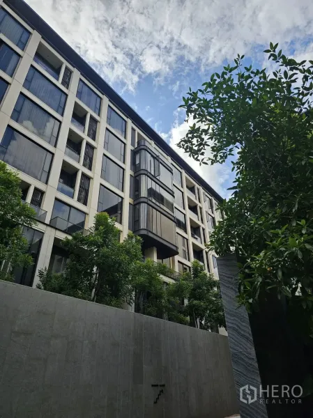 公寓 出租在Watthana, Bangkok - 瓦他那区低层公寓外立面，大窗与绿树映衬蓝天。