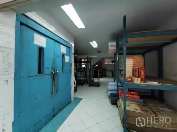 สำนักงาน ให้เช่าในKhlong San, Bangkok - พื้นที่เก็บของ ประตูเหล็กบานคู่สีน้ำเงิน และชั้นวางของโลหะ ใต้ไฟฟลูออเรสเซนต์