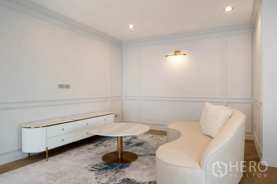 คอนโด ขายในBang Na, Bangkok - มุมนั่งเล่นอบอุ่น โซฟาโค้ง โต๊ะกาแฟกลม และตู้วางทีวีบนพรมลายสวย