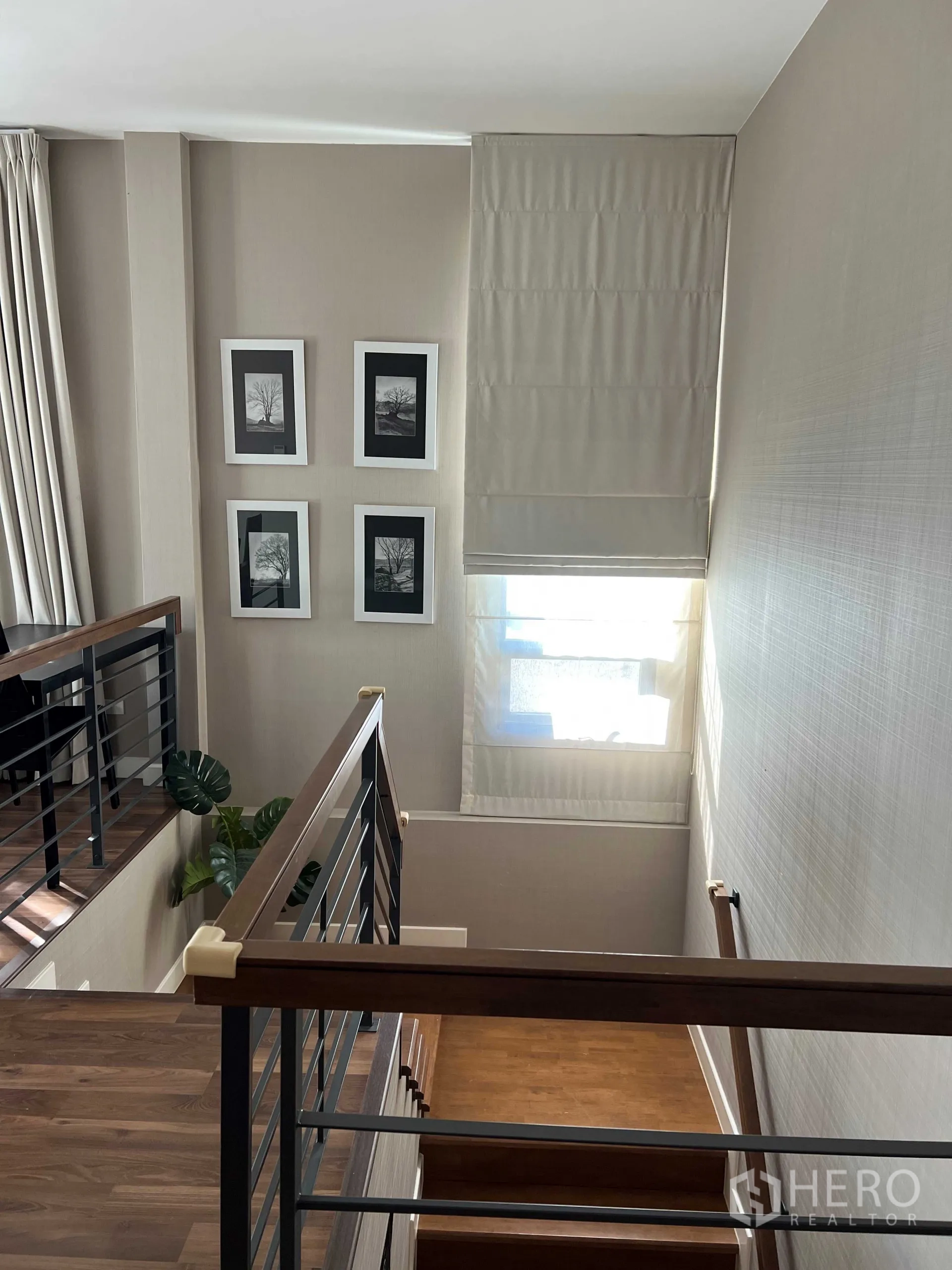 Detached House for rent in Prawet, Bangkok - Staircase landing with wooden steps, metal railing, framed art and a sunlit window.