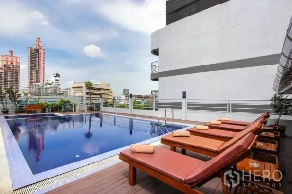 Apartment for sale in Ratchathewi, Bangkok - Rooftop pool deck with sun loungers and a Bangkok skyline backdrop.