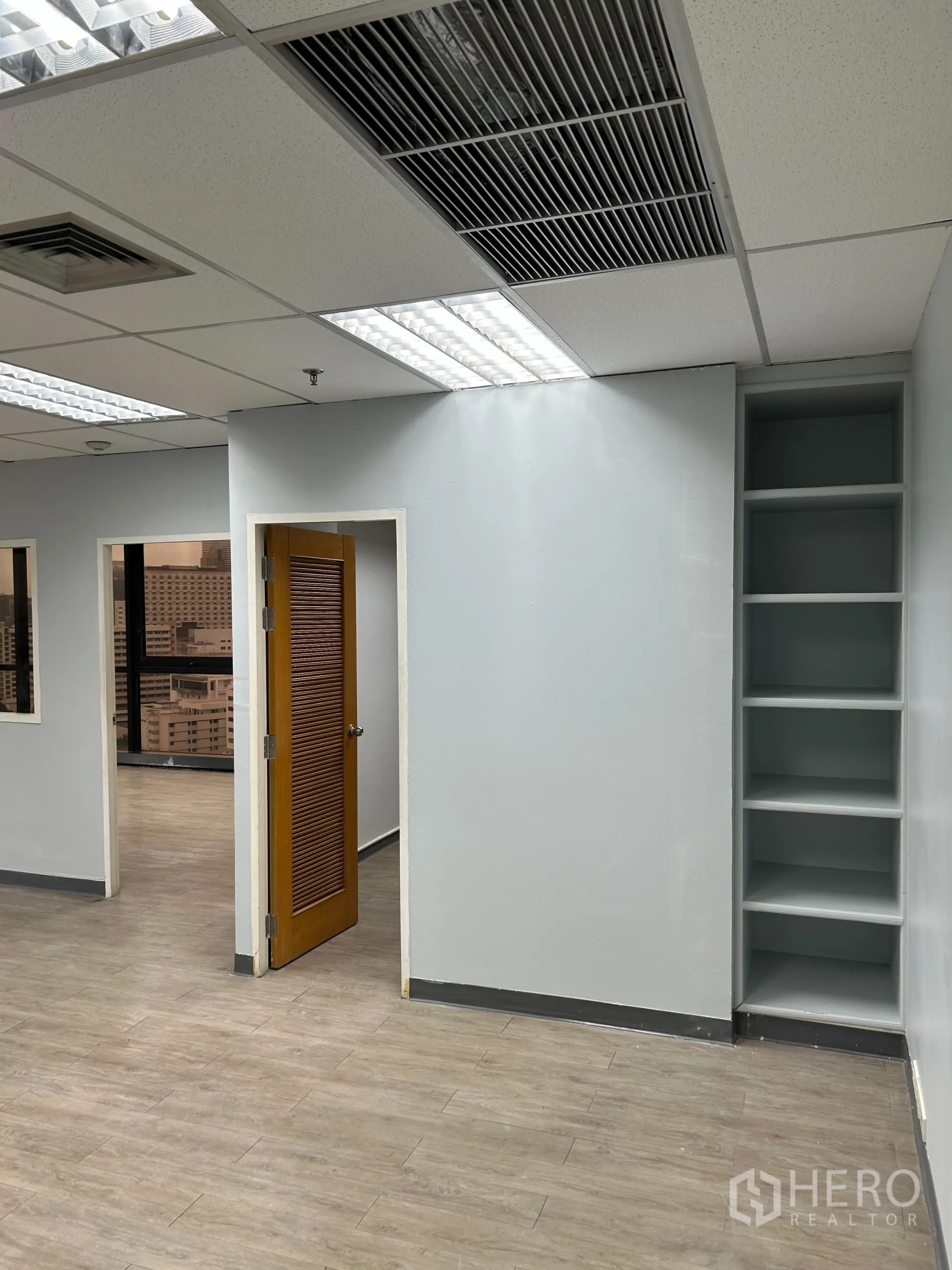 办公空间 出租在Khlong Toei, Bangkok - 内置开放式置物架与木门，顶部为空调出风口与照明。
