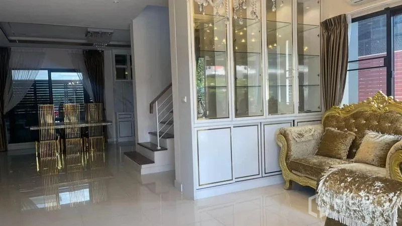 บ้าน ให้เช่าหรือขายในPrawet, Bangkok - ห้องนั่งเล่นสว่างพร้อมตู้โชว์กระจก โซฟาสีทอง และบันไดด้านข้าง