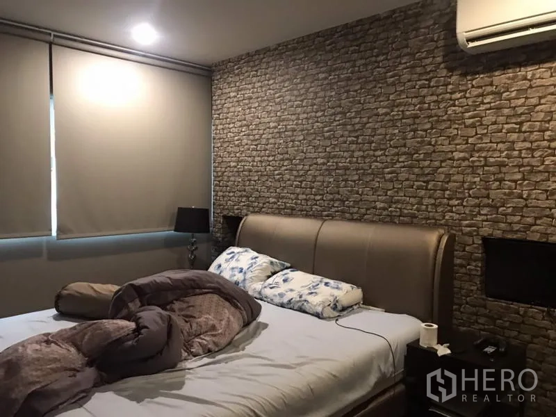 Townhouse for rent or sale in Suan Luang, Bangkok - Master bedroom with brick-pattern feature wall, upholstered bed, blackout blinds, and air conditioning.