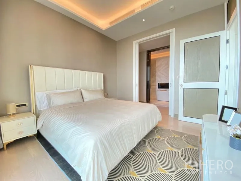 Condominium for rent in Khlong San, Bangkok - Primary bedroom with cove lighting and doorway to a luxurious ensuite bathroom.