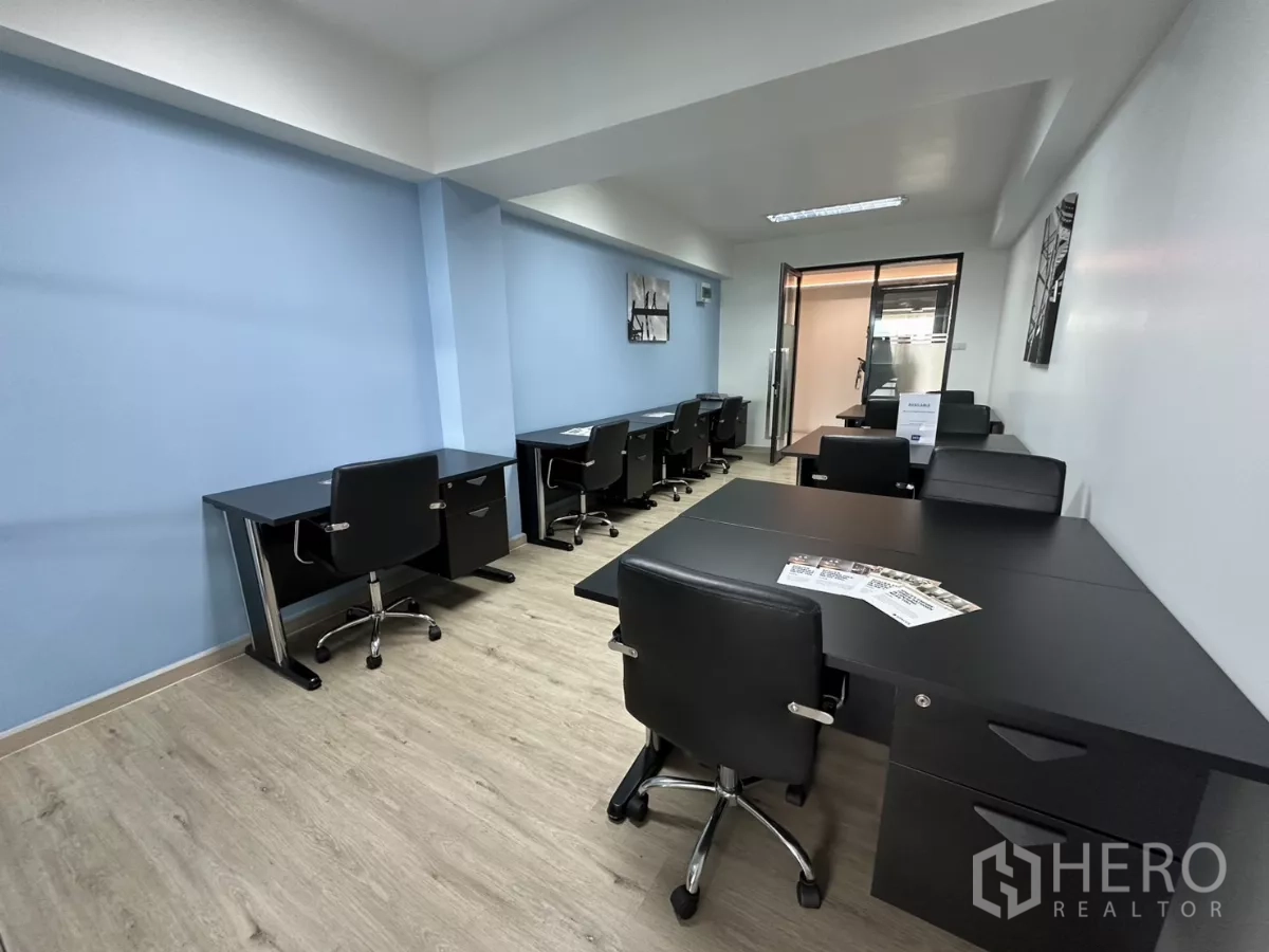 Office Space for rent in Watthana, Bangkok - Workstations along blue and white walls with light wood floors leading to a glass door meeting area.