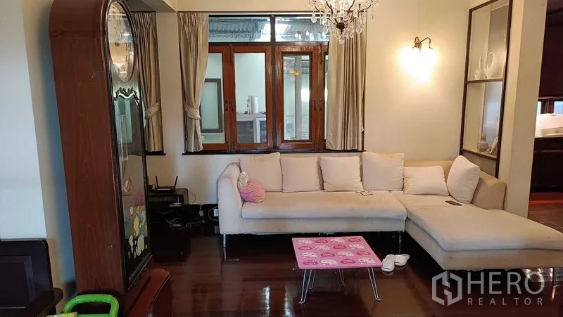 独立式住宅 出租在Phaya Thai, Bangkok - 舒适客厅，转角沙发、吊灯、木质窗与光亮木地板。