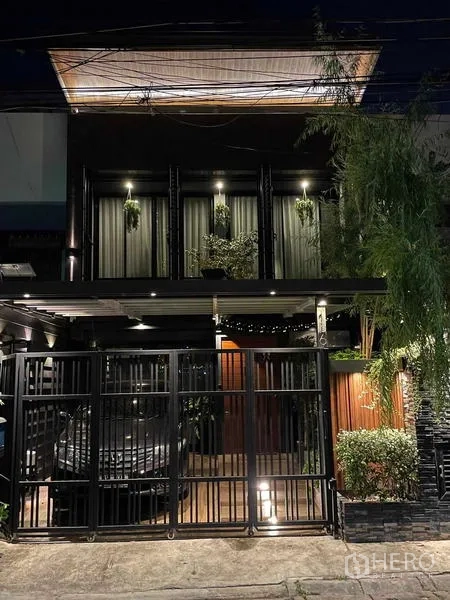 สำนักงานที่บ้าน ให้เช่าหรือขายในBang Kapi, Bangkok - ด้านหน้าโฮมออฟฟิศสองชั้นยามค่ำ มีกำแพงเหล็ก ที่จอดรถ และไฟส่องสว่าง