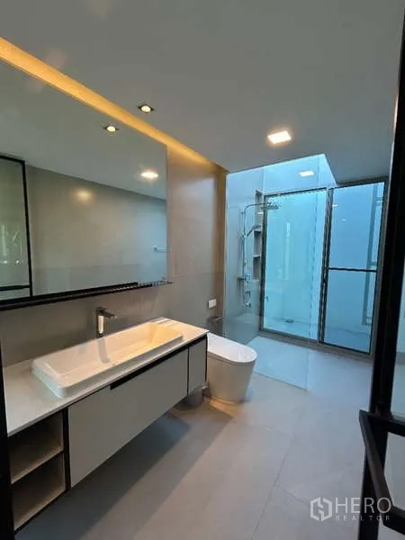 Detached House for rent in Saphan Sung, Bangkok - Contemporary bathroom with long vanity, large mirror and glass-enclosed shower.