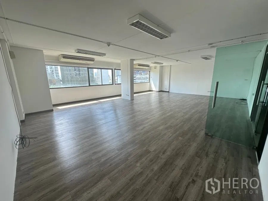 สำนักงาน ให้เช่า - มุมมองห้องทำงานว่าง พร้อมประตูกระจกกั้นห้อง พื้นสีไม้เข้ม แสงธรรมชาติทั่วถึง