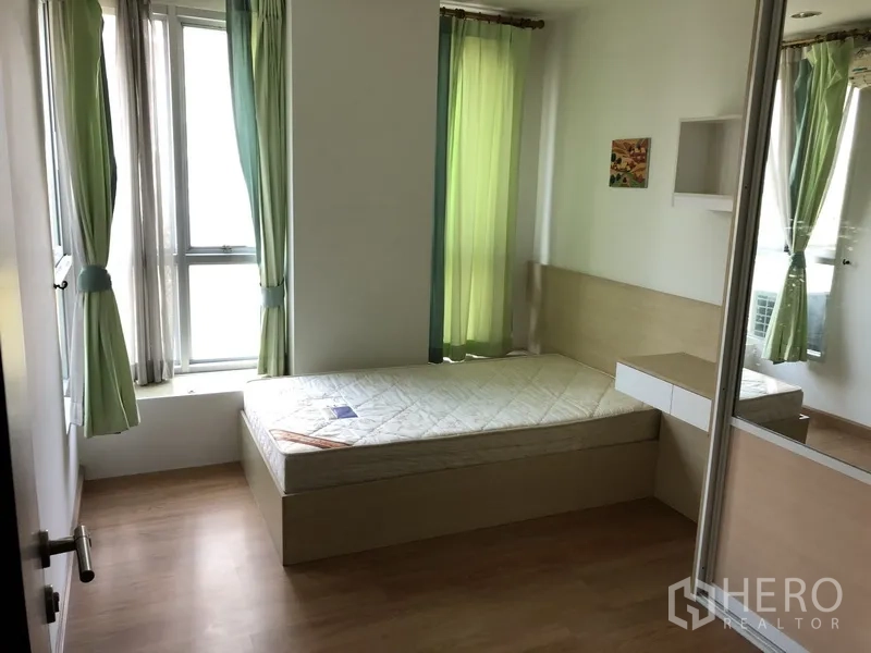 Condominium for rent in Khlong Toei, Bangkok - Sunny bedroom with single bed, green curtains, mirrored wardrobe, and large windows.