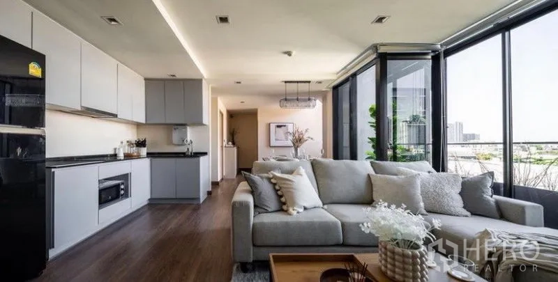 Condominium for rent or sale in Phra Khanong, Bangkok - Open kitchen with gray cabinetry flowing to the living area and wraparound floor-to-ceiling windows.