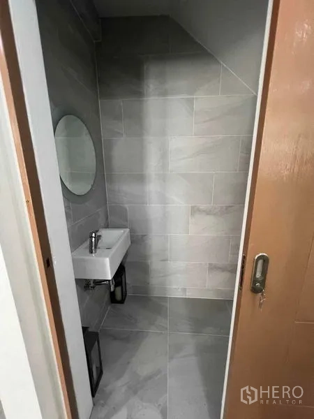 Townhouse for rent in Khlong Toei, Bangkok - Compact powder room under the stairs with wall mirror and small sink.