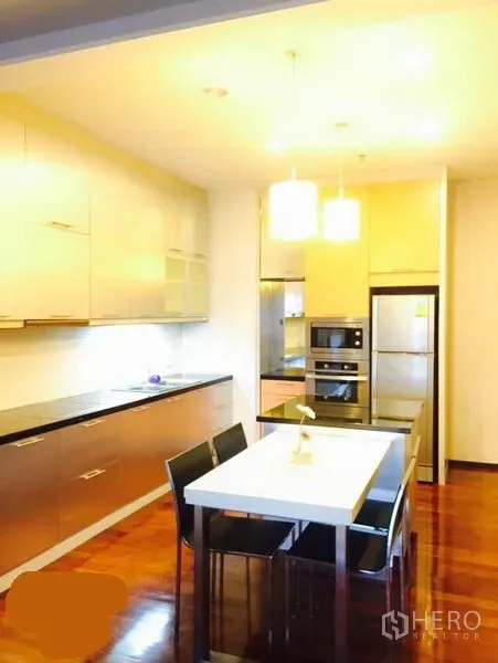 Condominium for rent in Watthana, Bangkok - Modern kitchen with long cabinetry, pendant lights, white dining table and black chairs, built-in appliances and wooden flooring.