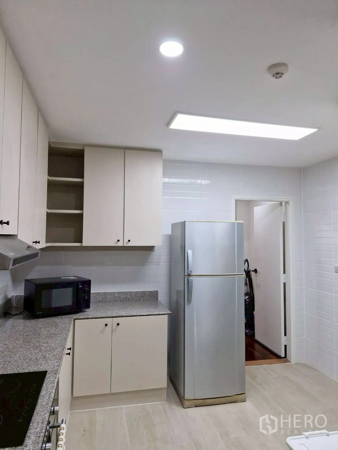 Condominium for rent in Khlong Toei, Bangkok - Kitchen area with tall refrigerator, microwave and ample storage cabinets.