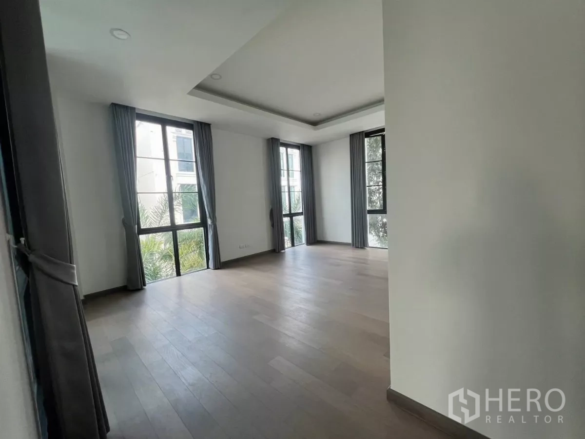 บ้าน ให้เช่าในLat Phrao, Bangkok - ห้องนอนมุมกว้าง พื้นไม้ หน้าต่างสูงพร้อมผ้าม่านสีเทา มองเห็นต้นไม้ภายนอก