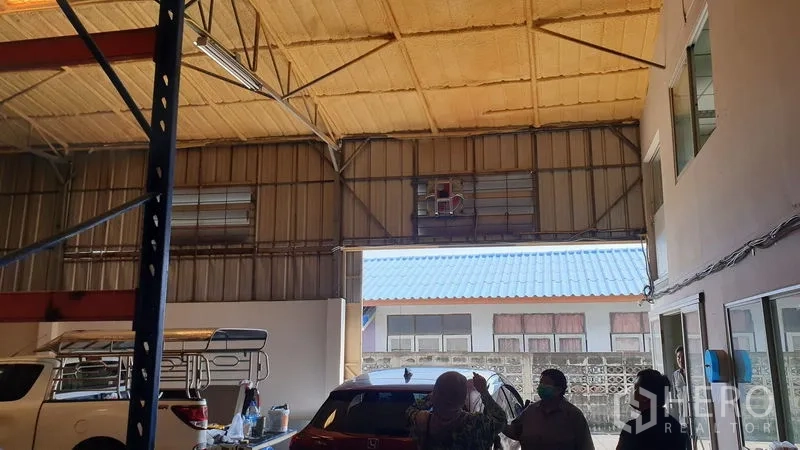 Warehouse for rent in Suan Luang, Bangkok - Warehouse entrance with high insulated roof, open bay and vehicles parked inside.