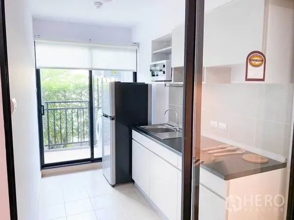 คอนโด ขายในKhlong Toei, Bangkok - ครัวแยกพร้อมตู้เก็บของสีขาว อ่างล้างมือ ตู้เย็น และประตูกระจกบานเลื่อนไปยังระเบียง