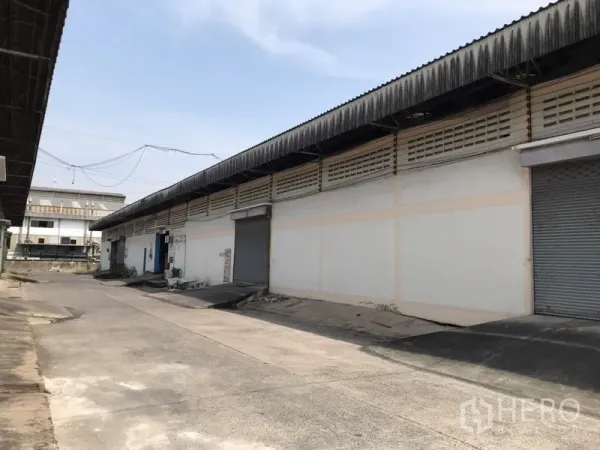 Warehouse for rent in Mueang Samut Prakan, Samut Prakan - Exterior of single-story warehouse with multiple roller shutter doors, raised loading ramps, and a wide concrete driveway.