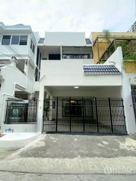 联排别墅 出租在Huai Khwang, Bangkok - 三层白色联排别墅外立面，带黑色金属大门和车库坡道