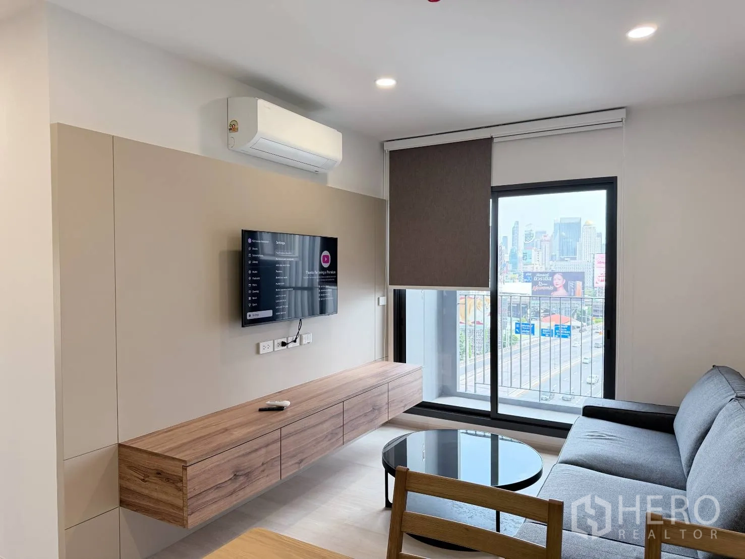 คอนโด for rent in Din Daeng, Bangkok - มุมนั่งเล่นอบอุ่นมีทีวีบนตู้คอนโซลลอย มู่ลี่ทึบแสง และราวระเบียงด้านนอก