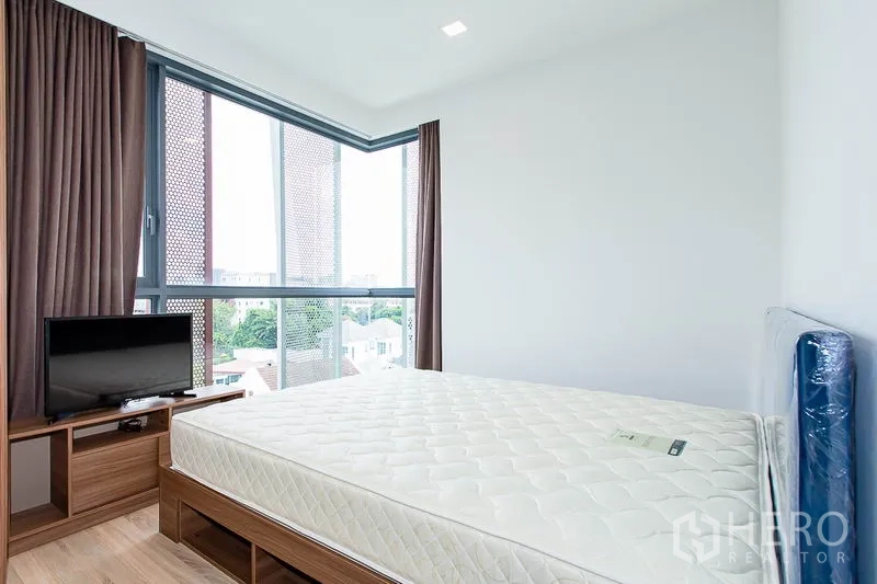 Condominium for rent in Watthana, Bangkok - Corner bedroom with large windows, TV console and new mattress offering green neighborhood views.