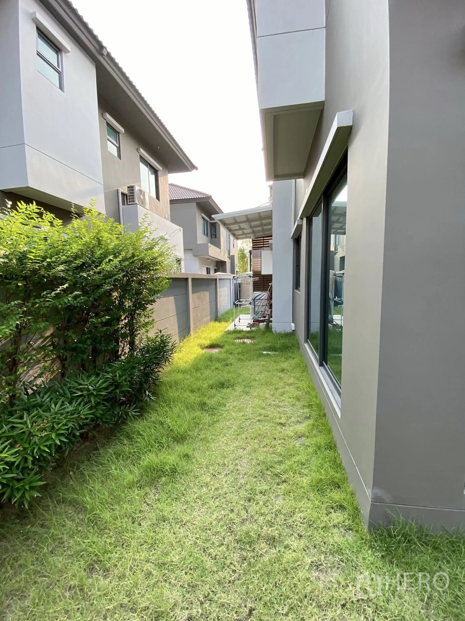 Detached House for sale in Saphan Sung, Bangkok - Side yard with green lawn and shrubs along the house exterior.