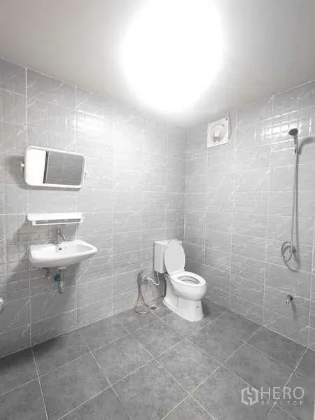 Warehouse for rent in Pak Kret, Nonthaburi - Clean tiled bathroom with toilet, sink, shower, and exhaust fan inside the unit.