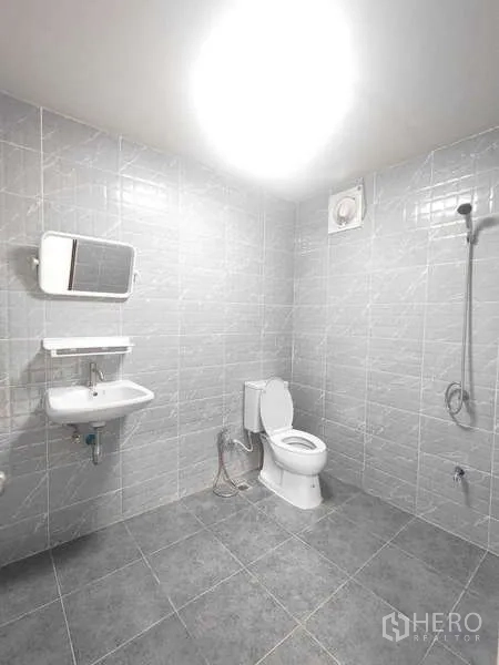 Warehouse for rent in Pak Kret, Nonthaburi - Clean tiled bathroom with toilet, sink, shower, and exhaust fan inside the unit.